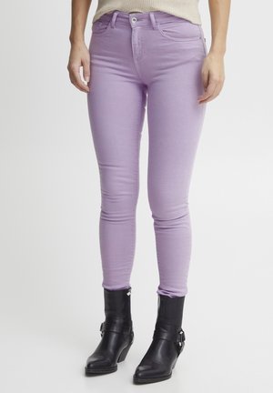 Jean skinny lavande avec une finition lisse, design à cinq poches et fermeture à bouton argenté, associés à des bottines noires.