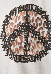 Hvid bomulds t-shirt med sort stiliseret tekst i et cirkulært mønster over et brunt leopardprint-design. Teksten fremstår fed og intrikat.