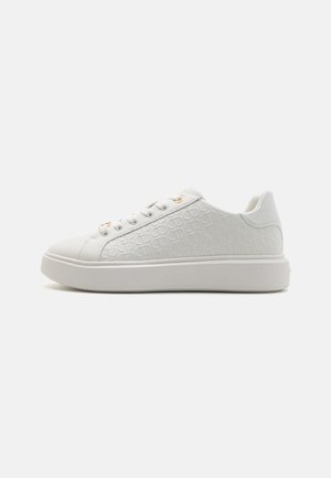 Witte sneaker met een gestructureerde bovenkant met reliëfprint, vlakke witte zool en zes veteropeningen met gouden accenten.