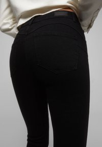 Svarta denimjeans med en åtsittande design, midja i normalhöjd, fem fickor och sömnadsdetaljer på bakfickorna.