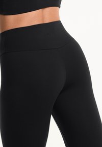 Fekete, magasan fines leggings sima, rugalmas anyagból. Zökkenőmentes derékkal és testhezálló fazonnal rendelkezik, aktív viselethez ideális.