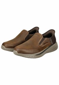 Slip-On-Schuhe mit einem Obermaterial aus braunem Leder, elastischen Seitenpanelen und einer strukturierten beige Gummisohle, die subtile Steppnähte aufweist.