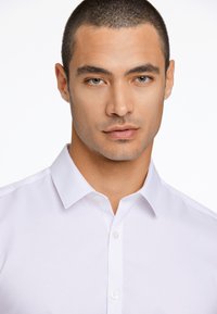 Witte overhemden met kraag, met een gladde textuur en een subtiele glans, weergegeven op een model met een neutrale achtergrond.