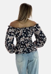 Off-shoulder blomsterbluse med smocket talje, lange ballonærmer, sort stof med beige og pink blomster mønstre.