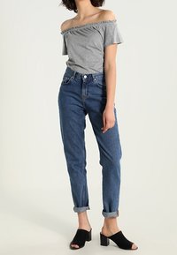 Gray off-the-shoulder top, light blue high-waisted jeans with rolled cuffs, and black block-heeled mules. Casual, fitted design.