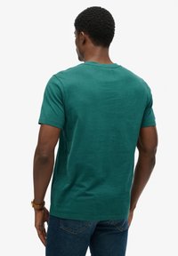 Koszulka z krótkim rękawem z głębokiej zielonej bawełny, z okrągłym dekoltem, prostym krojem i gładką fakturą. Minimalistyczny design bez wzorów i zdobień.