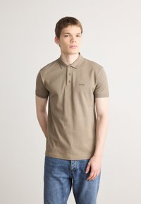 Bež majica polo s ovratnikom, kratkim rukavima i preklopom na tri gumba, s diskretno izvezenim logotipom na prsima.