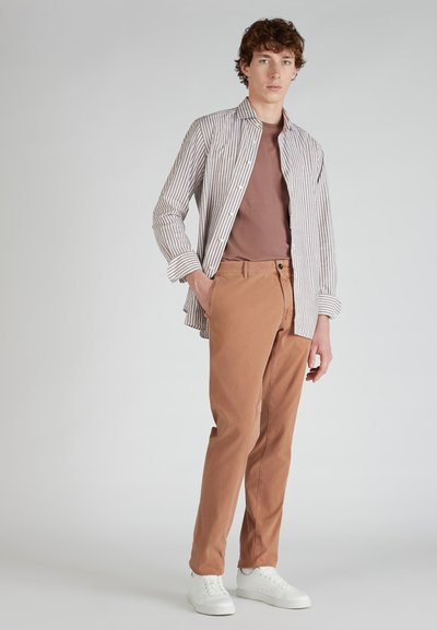 Koszula w paski w kolorze białym i granatowym, brązowa koszulka i spodnie w kolorze rdzy, połączone z białymi sneakersami. Gładki materiał, luźny fason.