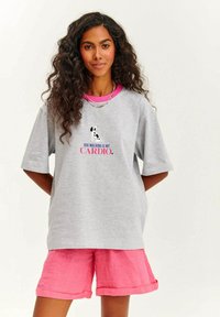 Šedé oversized tričko s krátkým rukávem, s grafikou černého psa a růžovým textem "VENČENÍ PSŮ JE MŮJ KARDIO." V kombinaci s růžovými šortkami.