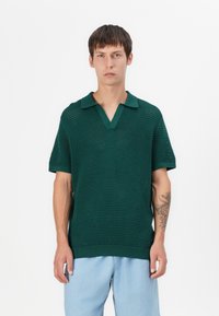 Polo shirt tricoté vert avec un motif texturé, à manches courtes et col, associé à un pantalon bleu clair.