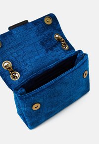 Modrá texturovaná látková taška s krokodýlím vzorem, zlaté kovové akcenty a otevřený vršek odhalující černý interiér.