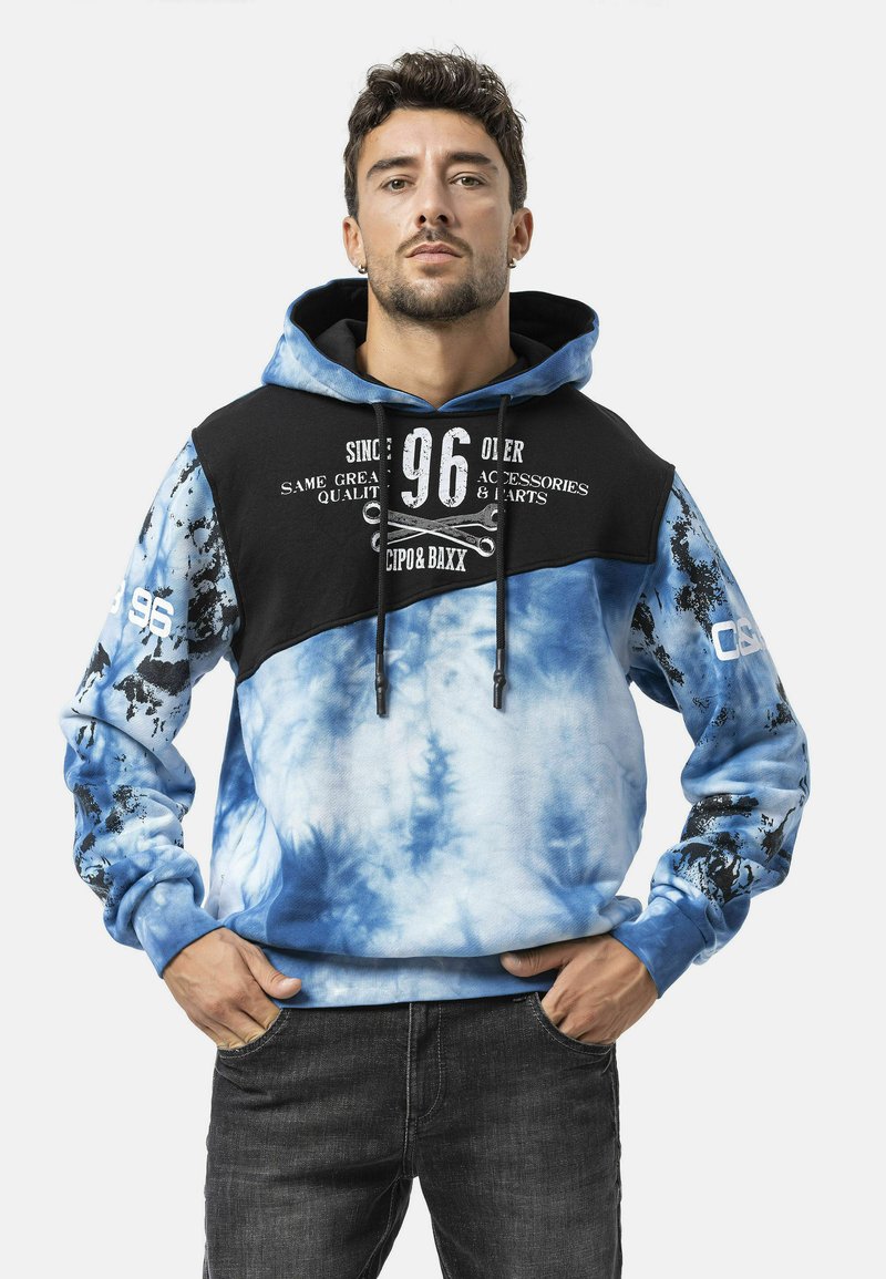 Capuchontrui met een zwart bovenstuk en een blauwe tie-dye onderkant. Heeft grafische tekst, verstelbare trekkoorden en een voorzak.