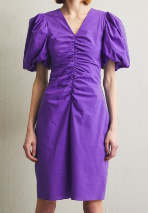 Purple dress with puff sleeves, V-neckline, and gathered detailing down the center. Smooth fabric with a structured shape.
