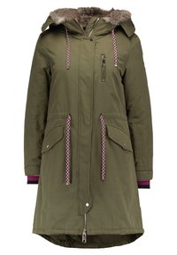 Parka verde oliva con capucha forrada de piel, cierre de cremallera en la parte delantera, dos bolsillos laterales y cordones en contraste. Presenta un dobladillo trasero más largo.