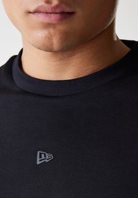 Black t-shirt with a round neckline and a small, grey logo on the chest. The fabric appears smooth and fitted.