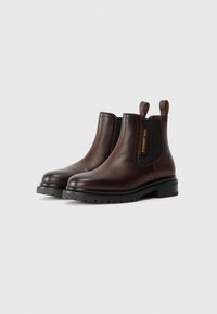 Bottes Chelsea en cuir marron avec des panneaux élastiques sur les côtés, des languettes de tirage et une semelle en caoutchouc texturé noir. Présente une étiquette de logo sur le côté.