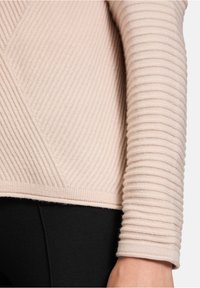 Krämfärgad ribbad tröja med diagonala och vertikala texturmönster. Mjuk, stickad tyg med en figurnära design.