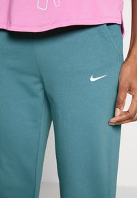 Tealfarbene Sweatpants aus weichem Material, mit einem weißen Nike-Logo auf dem Oberschenkel, elastischem Bund und seitlichen Taschen.