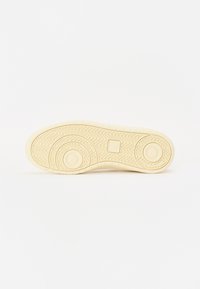 A világoskrém színű sneaker talpja zig zag mintázattal és kör alakú bordázott részletekkel rendelkezik, sima textúrával és lekerekített szélekkel.