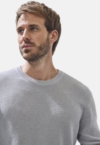 Grau gestrickter Pullover mit gerippter Textur, runden Halsausschnitt und langen Ärmeln. Der Stoff wirkt weich und leicht.