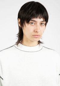 Pull en tricot blanc avec un col montant, arborant une ligne d'accent noir le long de l'encolure et des épaules. Texture lisse, coupe décontractée.