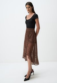 Haut noir à côtes avec un décolleté en scoop associé à une jupe asymétrique à imprimé léopard marron, portée avec des chaussures à talons hauts noires.