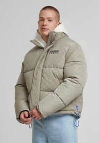 Puffjakke i lys grå med en blank finish, der har et prægede mønster, lynlås lukning og snoretræk ved kanten.