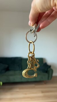 Chaveiro de latão com um grande fecho em forma de gancho, várias chaves e um anel de chave circular. Acabamento texturizado e curvas suaves.