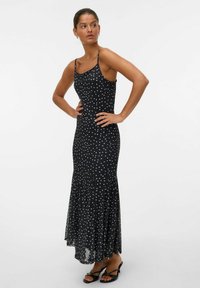 Robe noire à pois avec un corsage ajusté, un ourlet fluide, des bretelles fines et un bas évasé. Le matériau semble léger et lisse.
