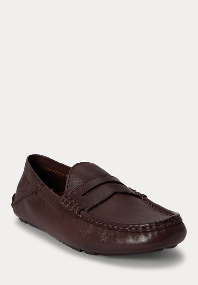 Καφετί δερμάτινο μοκασίνι με ραμμένες λεπτομέρειες και ομαλή στρογγυλεμένη μύτη, τοποθετημένο σε λευκό φόντο.
