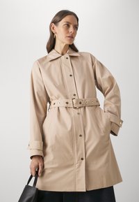 Palton bej realizat dintr-un material neted, având talie îmbrăcată, accesorii din metal auriu, nasturi mari și buzunare laterale.