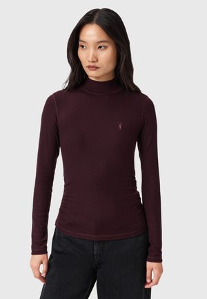 Langsleeve coltrui in diep bordeaux met een aansluitend ontwerp en subtiele plooien bij de taille. Voorzien van een klein geborduurd logo op de borst.