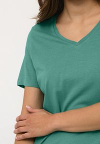 Tyrkysové tričko s výstřihem do V a krátkým rukávem, vyrobené z měkké bavlněné tkaniny, s hladkou texturou a volným střihem.