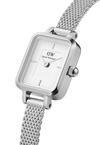 Montre carrée en argent avec un cadran blanc, indicateurs horaires simples et un bracelet en métal tressé. Présente une couronne ronde et un design minimaliste.