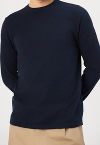 Marineblaue Langarmshirt aus weichem Stoff mit Rundhalsausschnitt. Hat eine schlanke Passform und dezente gerippte Bündchen und Saum.