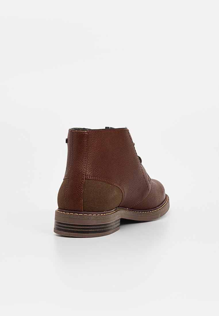 Brązowy skórzany boot na kostkę z teksturowaną powierzchnią, kontrastową panelą z tkaniny, zaokrąglonym czubkiem i zbudowanym obcasem. Widoczne detale szwów.