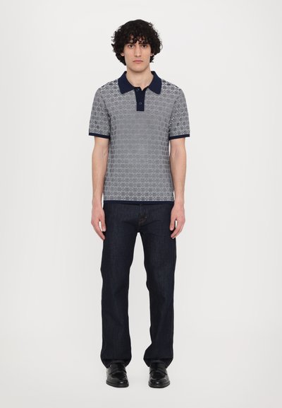 Šedé vzorované polo tričko s námořnickým límečkem, doplněné tmavými džíny. Tričko má jemný geometrický design. Černé boty.
