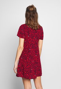 Vestido rojo con mangas cortas, que presenta un estampado de pequeños corazones negros. Corte en A, tejido ligero y escote redondeado.