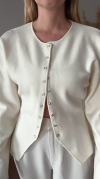Cardigã de cor creme feito de material macio, com decote arredondado, botões prateados na frente e bainha ligeiramente curta.