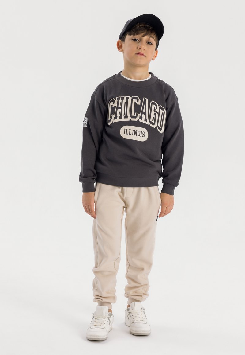 Grijze sweatshirt met de opdruk "Chicago" en "Illinois", beige sweatpants, witte sneakers en een zwarte pet. Zacht, casual ontwerp, relaxte pasvorm.