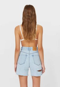 Shorts de mezclilla azul claro con cintura alta, dobladillo deshilachado y un desgarro en la pierna derecha. Cuenta con una etiqueta de cuero en la pretina trasera.