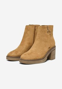 Bottines en suède beige à bout arrondi, avec des zips latéraux et des talons bloc texturés. Comprend un accent matériel circulaire.