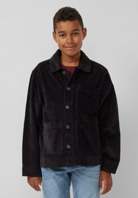 Schwarze Cordjacke mit Kragen, Frontknöpfen, zwei Taschen und lockerer Passform, kombiniert mit hellblauen Jeans.