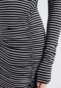 Gestreiftes Kleid mit horizontalen schwarzen und grauen Linien, langen Ärmeln und gerafften Seitendetails, hergestellt aus einem weichen, elastischen Stoff.