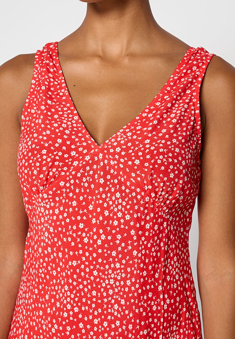 Abito rosso floreale con scollatura a V e spalline larghe, realizzato in un tessuto leggero, con piccoli pattern di fiori bianchi e un corpetto aderente.