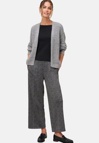 Lichtgrijze gebreide cardigan, zwart top met korte mouwen, gebloemde wijde broek in zwart en grijs, zwarte instappers, met zakken in de cardigan.