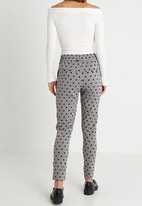 Grijze polkadotbroek met een taps toelopende pasvorm en elastische tailleband, gecombineerd met een witte off-shoulder geribbelde top en zwarte schoenen.