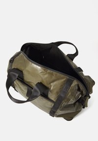Maslinzasta duffel torba s velikim otvorom, izrađena od izdržljivog materijala. Ima čvrste crne trake i glatku, sjajnu vanjštinu.