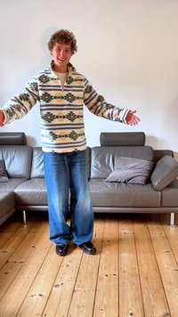 Pulôver de pele texturada com um padrão em creme, verde e azul. Par de jeans azuis claros de cintura larga e sapatos pretos.