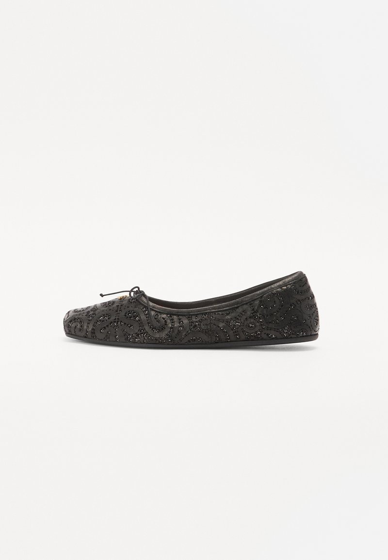 Black ballet flat made of fabric, featuring an intricate embossed pattern, a rounded toe, and a decorative bow at the front.